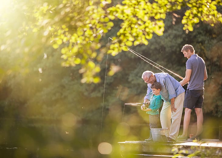 Boy, father, and grandfather fishing in lake.