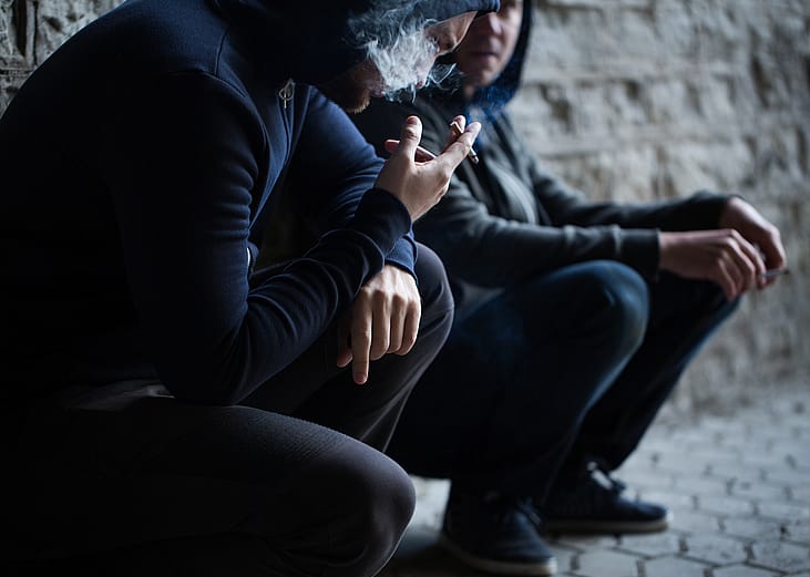 Close up of two young men smoking cigarettes outdoors.