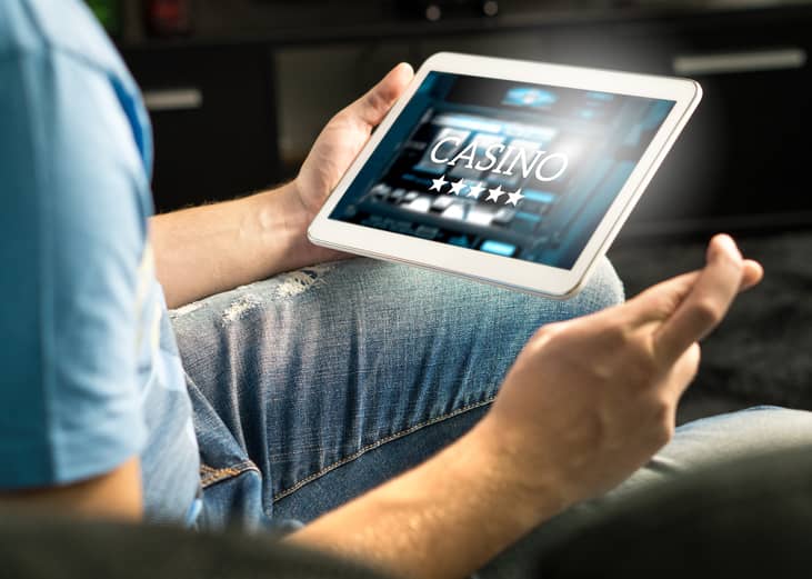 Man playing in an online casino with tablet, fingers crossed.