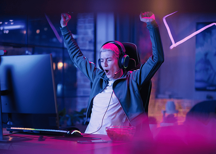 A person cheering at a computer in a dim room with neon lights.