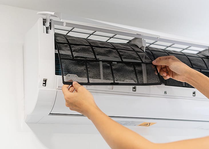 Person pulling out a dirty air conditioner filter from a mini-split unit.