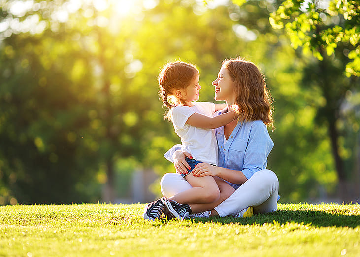 A mother with her young daughter sitting on grass in a nature park.