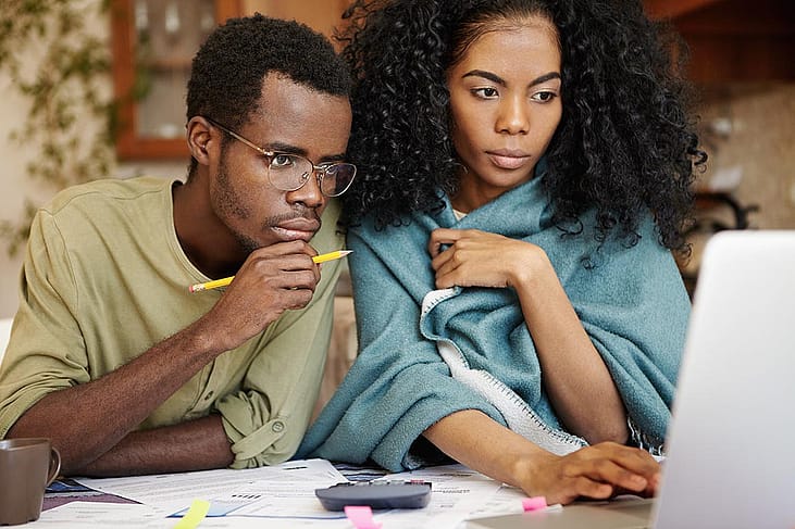 Young Black couple looking over laptop screen with papers and a calculator sitting on the table