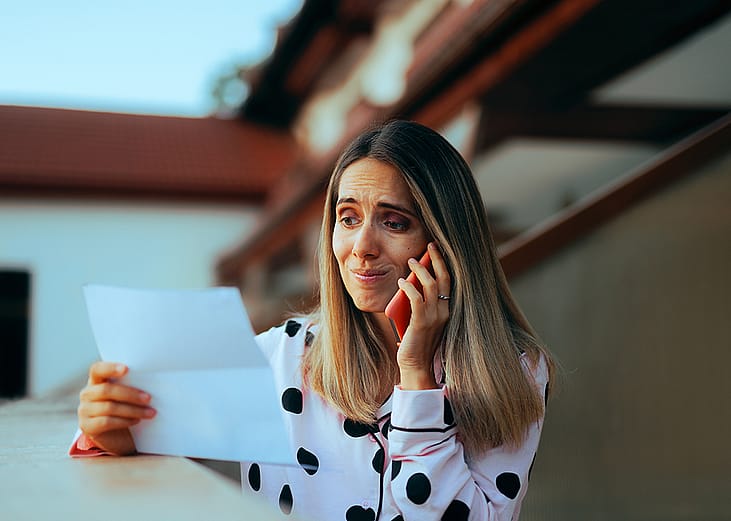An emotional woman looking at her credit card bill while on the phone.
