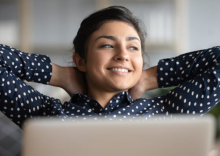Satisfied woman happily sitting  at work with her hands behind her head.