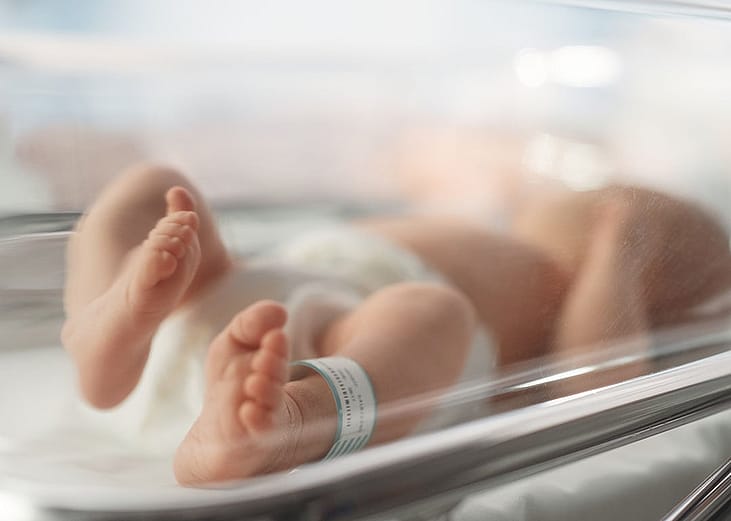 Newborn baby lying in bassinet in hospital with toes and feet in focus.