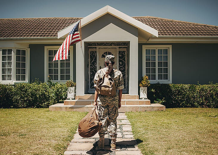 Female veteran soldier with luggages coming home and standing in front of her house.