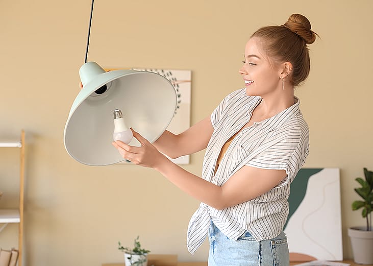Young woman screwing light bulb into a ceiling lamp.
