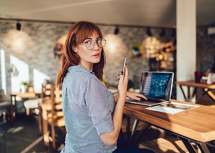 Woman looking at the camera while dialing a number on her mobile phone.