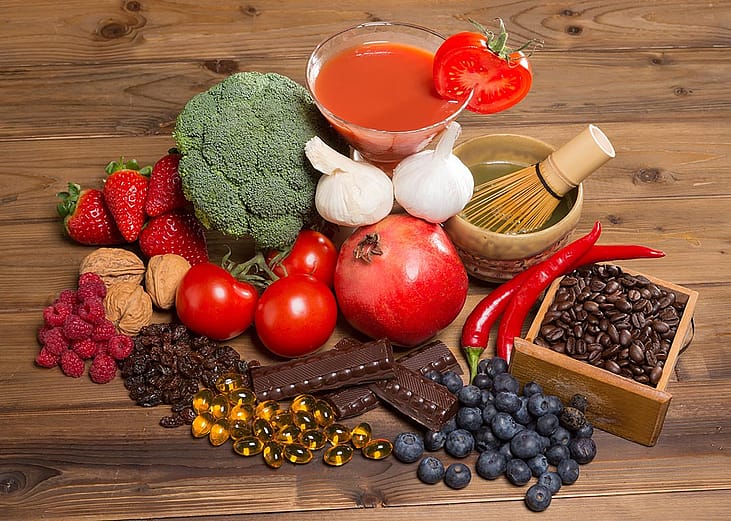 Healthy antioxidants foods like broccoli, berries, tomoatoes, pomegranates, green tea, coffee, nuts and chocolate  on a wooden table.