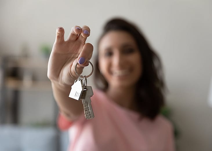 A young female homeowner holding up the keys to her house.