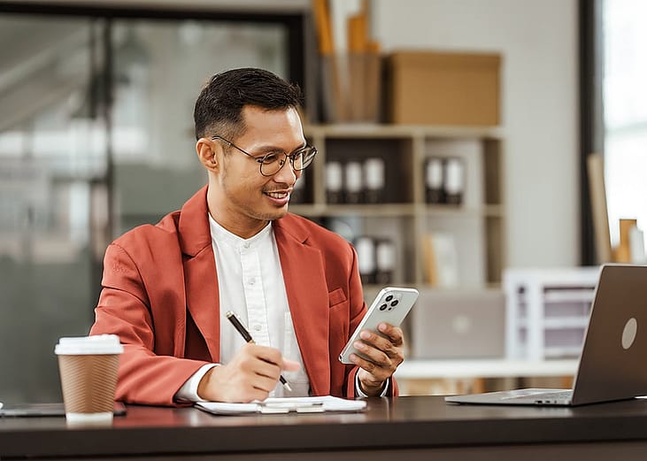 Small business owner holding a phone on his one hand and writing down information with the other.