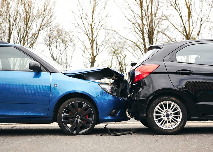 Two cars involved in traffic accident on side of the road with damage to hood and fender.