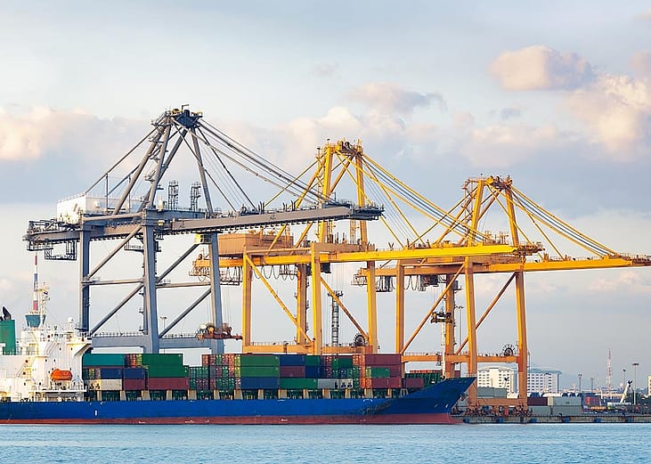 Two yellow and one gray crane with a cargo ship in a port.