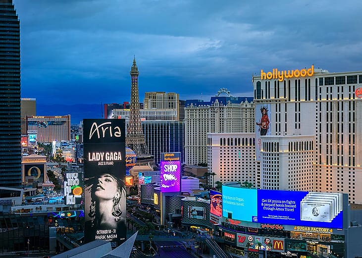 The Strip skyline in Las Vegas with advertising billboards including Lady Gaga, neon lights on iconic hotels and casinos after sunset.