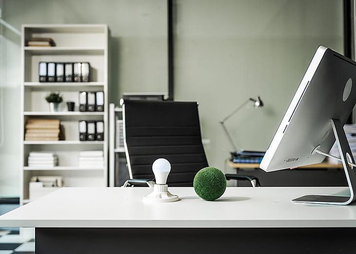 A modern empty office with a vacant chair behind a desk with a computer monitor and desktop decor.