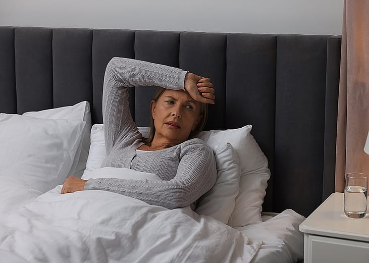 A middle-aged woman experiencing headache while sitting on bed.