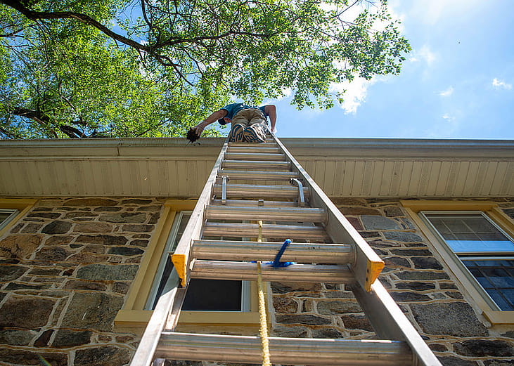 Low angle view of a man on a ladder cleaning a home's gutters.