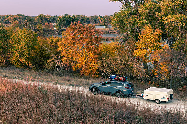 A blue 2020 Honda CR-V towing a 1990 Coleman Columbia pop-up camper on the road towards Antelope Lake in Kansas during autumn.