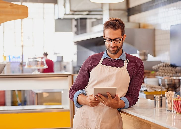 A coffee shop owner using a tablet inside the shop's kitchen.