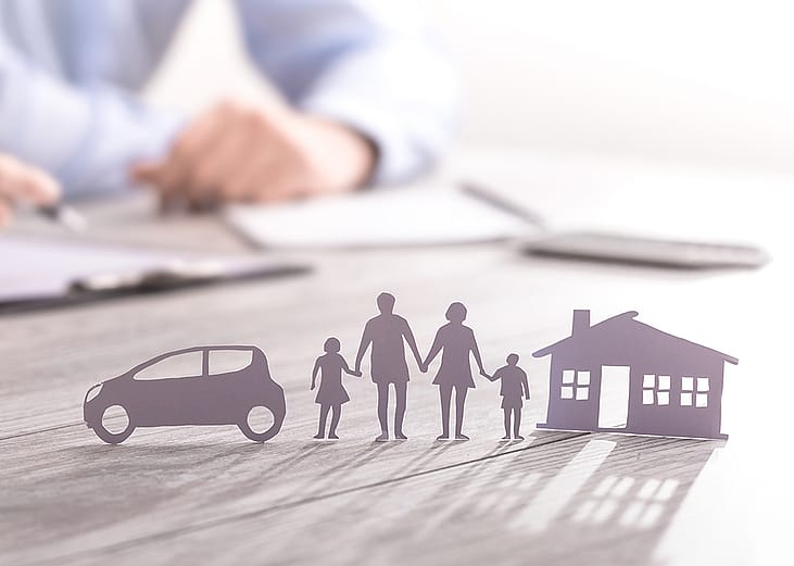 an insurance agent writing in documents with a paper figure of a family with a house and car.