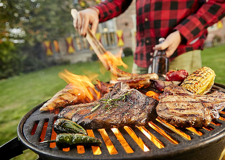 Assorted meat like sausages and steak with vegetables being grilled on a BBQ grill outdoors.