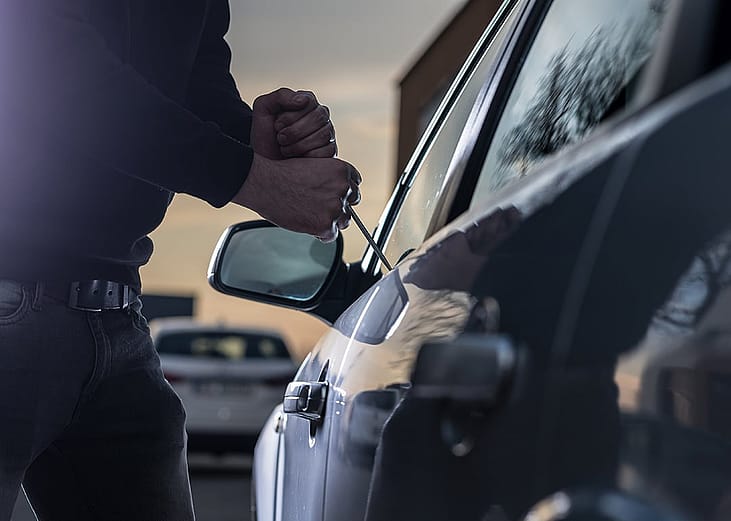 A thief trying to break into a car window with a screwdriver.
