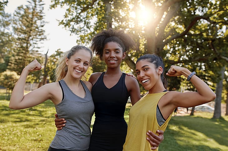 Three women flexing their muscles in a park.