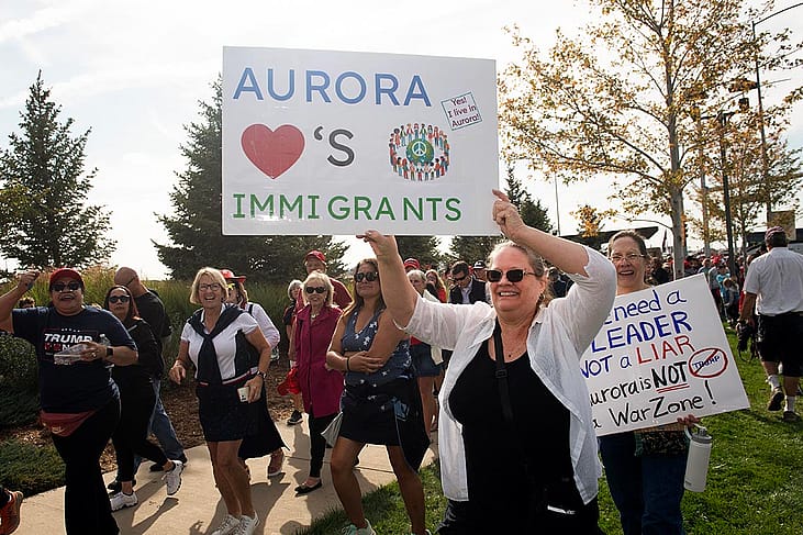 People in Denver protesting the federal government's stance on immigration; one holds a white posterboard that reads "Aurora loves immigrants"
