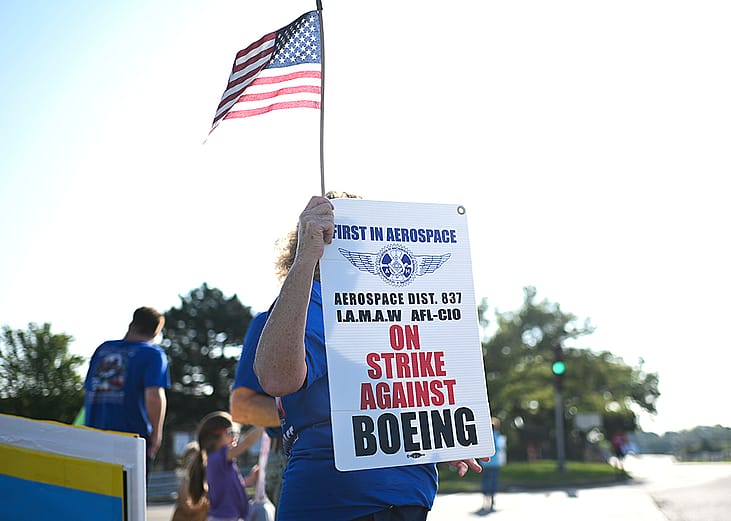 Boeing defense plant workers holding up "Strike Against Boeing" signs outside of a Boeing facility in Berkeley, Missouri.