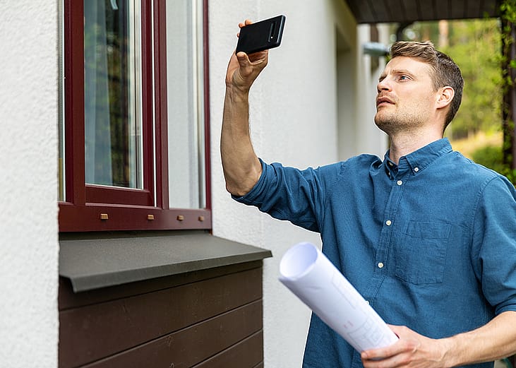 A real estate appraiser takes photo of the outside of a property with his phone.