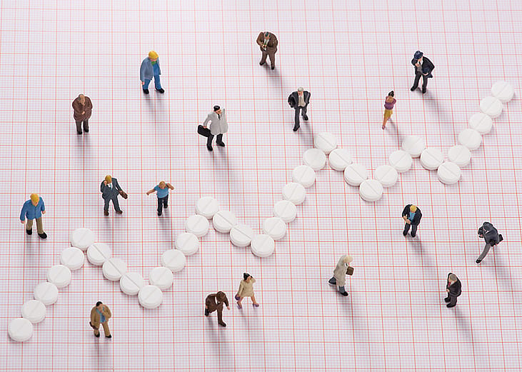 White pills forming a jagged line, dividing small figures of different people to represent different healthcare costs among groups.
