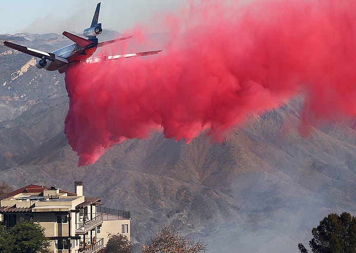 A firefighting aircraft drops the fire retardant Phos-Chek near homes during the Palisades Fire on January 10, 2025 in Topanga, California.