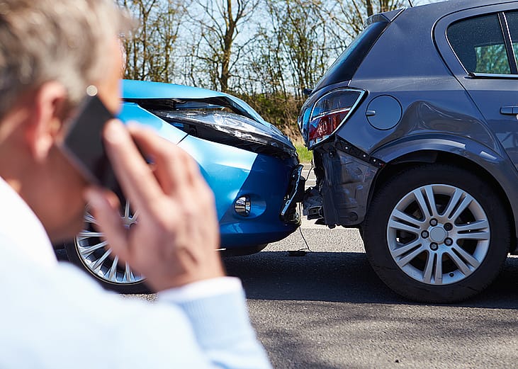 A car driver talks on the phone while looking at a rear-end collision.
