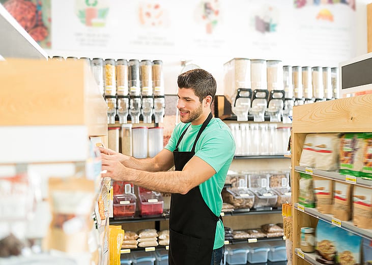 A zero-waste grocery store owner arranging stock of items on shelves.