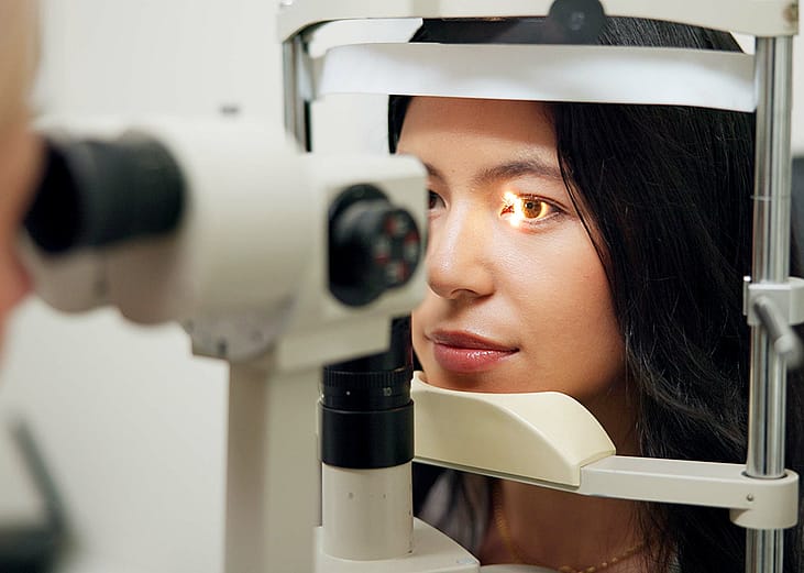 A woman in front of a slit lamp as an eye specialist takes her vision test.