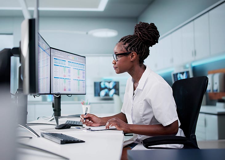 A hospital staff looking at spreadsheets and billing codes using desktop with multiple monitors.