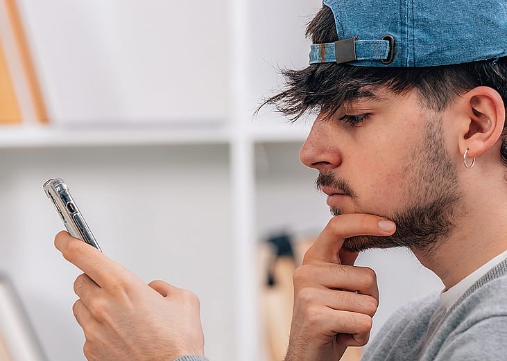 A young man looks at his smartphone pensively.