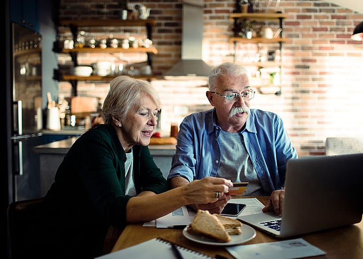 An elderly couple using a credit card at home with a laptop.