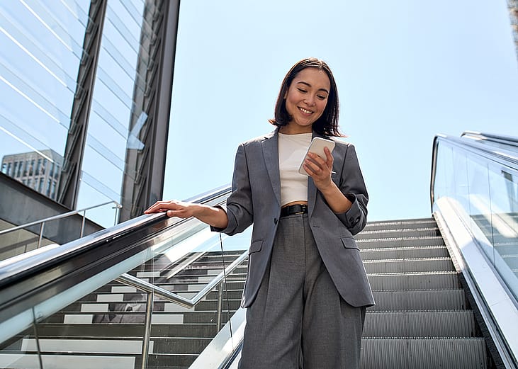 A young female marketing professional smiling at her phone while standing on an escalator.