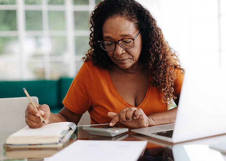 An elderly black woman calculating finances at home.