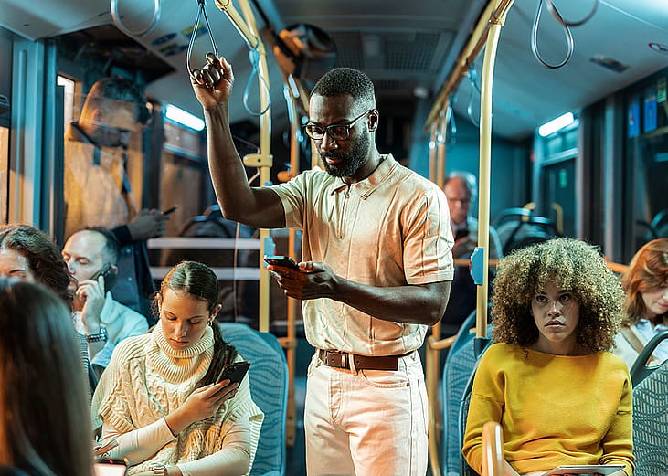 A young black man standing in a crowded bus at night.