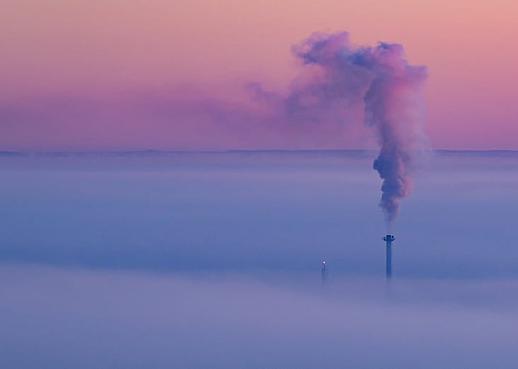 Smoke coming out of a heat and power plant chimney, blending with a lavender morning sky.