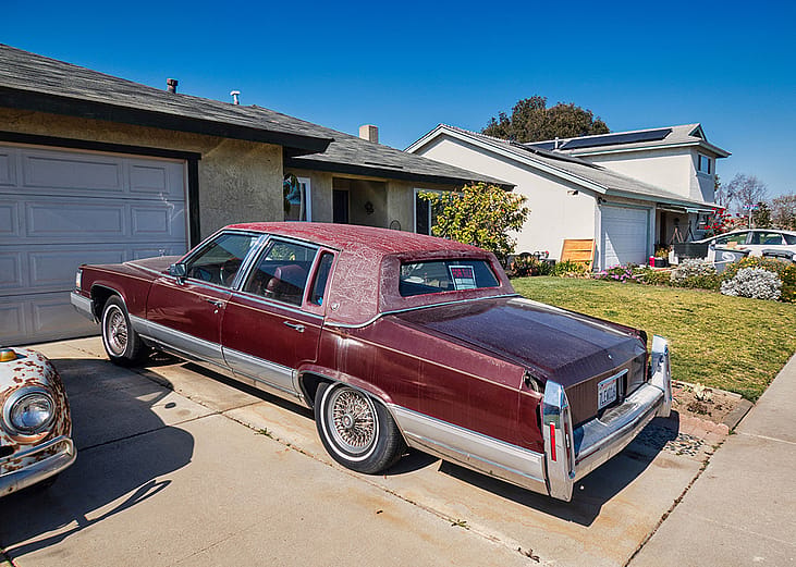An old red vintage car parked on the driveway of a home.