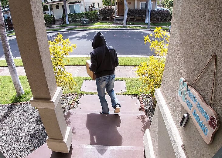 A surveillance camera-view of a package thief walking away from a porch after taking a package.