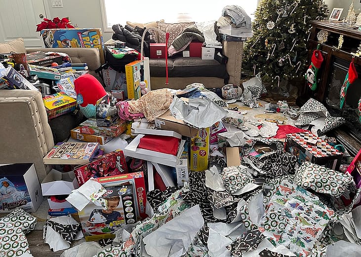 Piles of messy packaging and opened presents in a living room during Christmas morning.