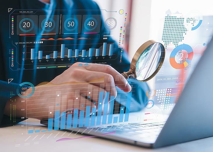 Person holding a magnifying glass close to a laptop screen, illustrated with data charts and graphics.