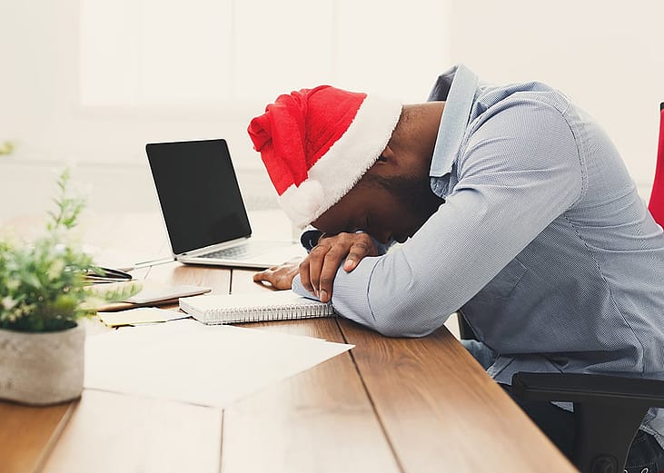 A tired businessman wearing a Christmas hat while asleep at work.