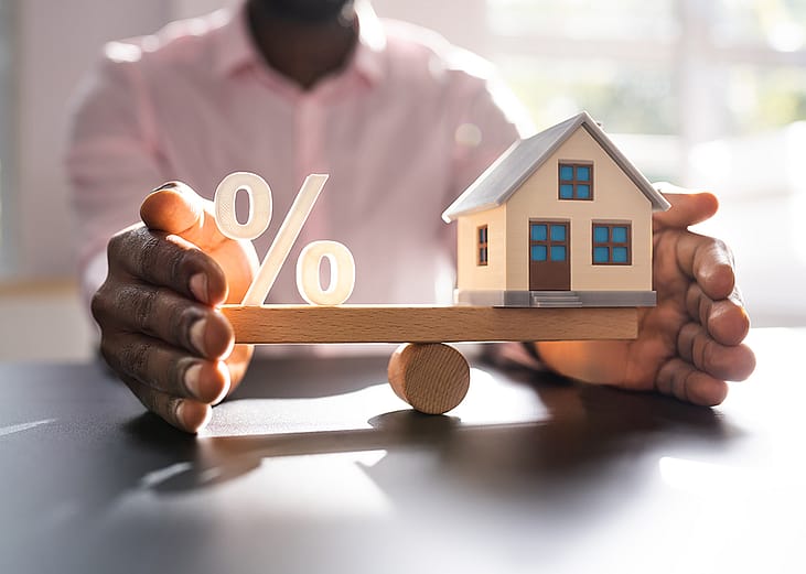 A person balancing figures of a percentage and a small house.