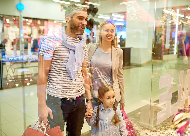 A happy family looking at window displays while shopping at a mall.